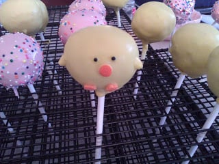 pink sprinkles and yellow chick cake pops drying on a wire rack