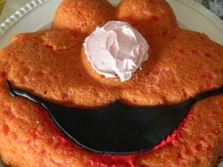 frosting on the nose of elmo cake and black fondant placed on his mouth