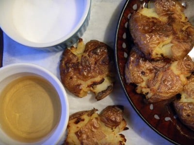 Top down photo of smashed potatoes on a plate, with two next to the plate. 