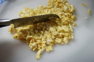 cooked scrabbled eggs being chopped on a cutting board