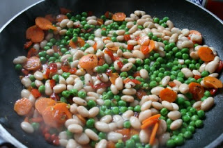 peas and white beans being added to vegetable mixture in frying pan