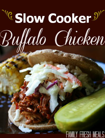 Slow Cooker Buffalo Chicken - FamilyFreshMeals.com Side photo of the Slow Cooker Buffalo Chicken served on a bun and topped with cole slaw. On the side is a pickle and corn on the cob