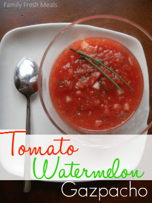 Top down photo of gazpacho in a glass bowl, sitting on a plate with a spoon