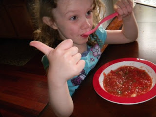 child sitting at a table giving a "thumbs up" while eating the Tomato Watermelon Gazpacho