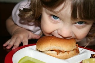 child biting into sandwich that is sitting on a plate