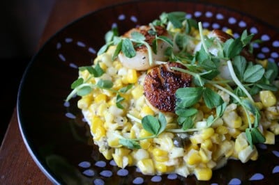 Creamed Corn and Scallops served on a dark plate and topped with peashoot