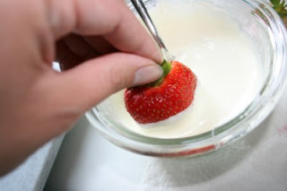 strawberry being dipped in to melted white chocolate
