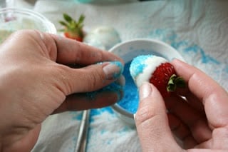 adding light blue sugar sprinkles to the lower part of strawberries