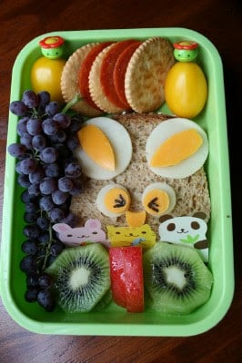 funny face sandwich packed in a lunchbox with fruit, cheese and crackers