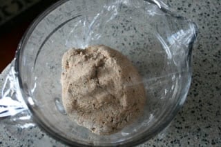 dough in a glass bowl, covered with saran wrap