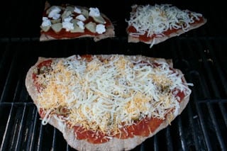 pizza sauce, cheese and topping add to the top of the dough on the grill