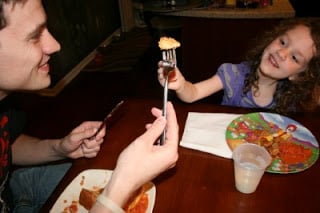 man and child holding a piece of pizza pie on their forks