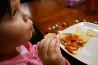 child sitting at a table with a plate of pizza dip and tortilla chips