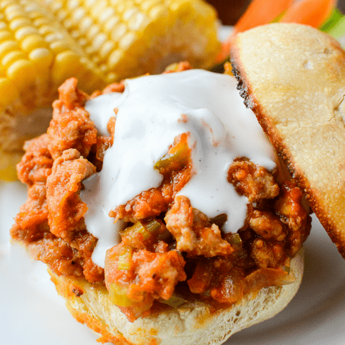 Buffalo Sloppy Joes served on a toasted bun, with corn on the cob on a white plate