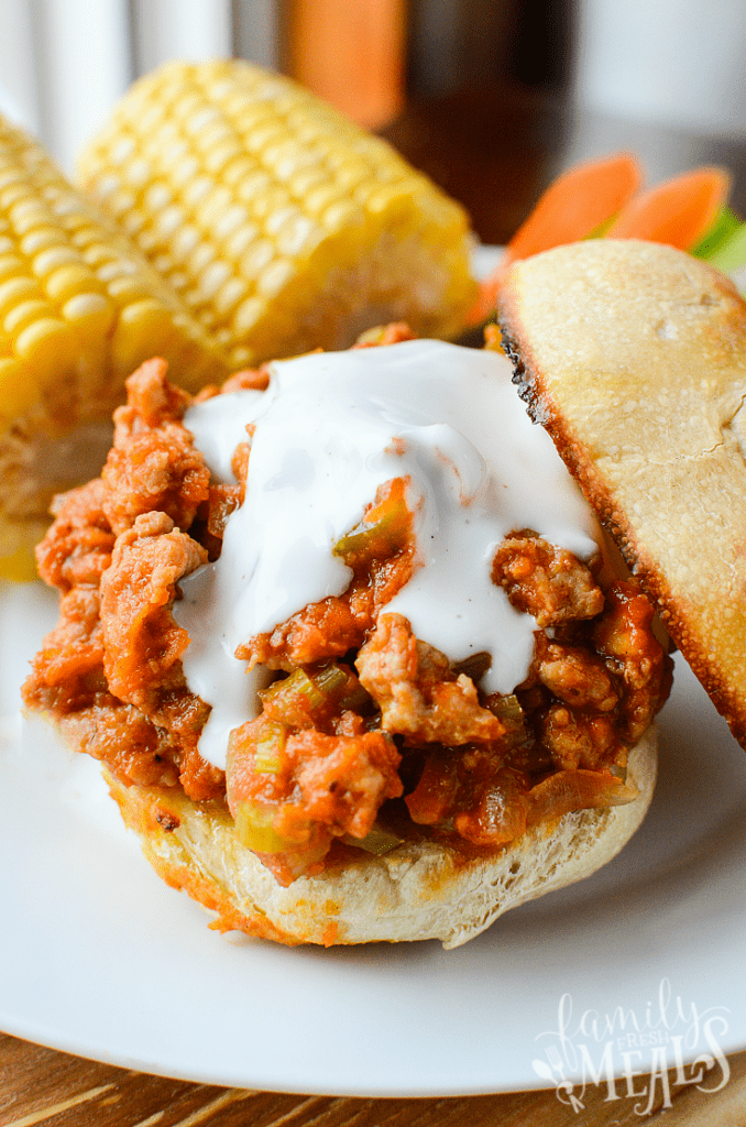 Buffalo Sloppy Joes  served on a toasted bun, with corn on the cob on a white plate