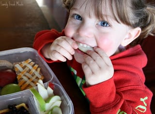 Child sitting at a table eating the A Tisket, A Tasket lunchbox