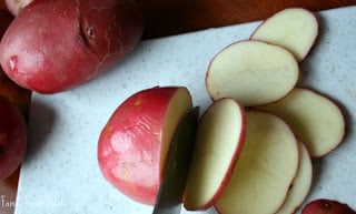 red potatoes being sliced on a cutting board