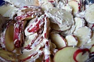 mixing sliced red potatoes in with creamy mixture