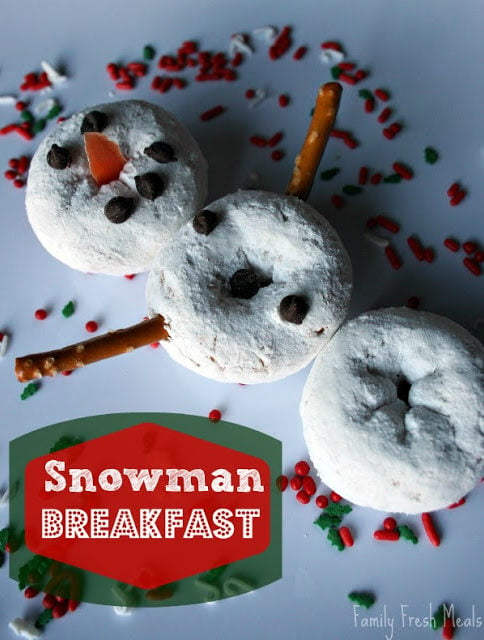 Snowman made of powdered mini donuts, pretzels and mini chocolate chips, on a white plate, surrounded by holiday food sprinkles