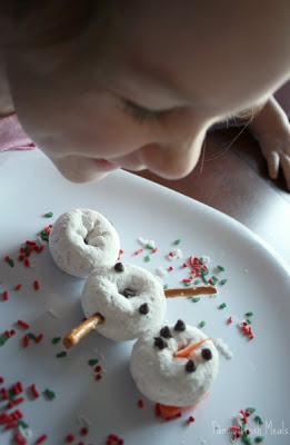 child sitting at a table, looking and smiling at donut snowman