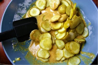 Pickle slices being mixed in a bowl with sauce