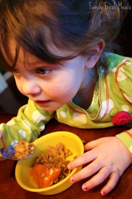 small child eating a stuffed pepper at a table