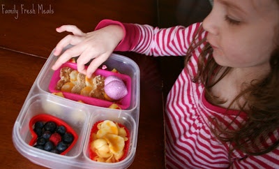 Child sitting at a table eating heart shaped food from lunchbox 