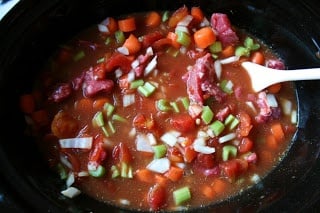 Crockpot Irish Stew in a black slow cooker being stirred with a wooden spoon