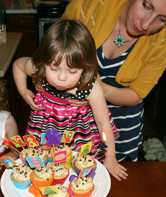 woman holding child while she blows out candles on cupcakes