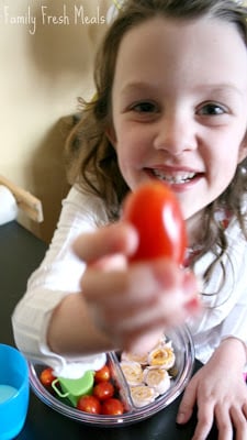 child holding up a cherry tomato to the camera