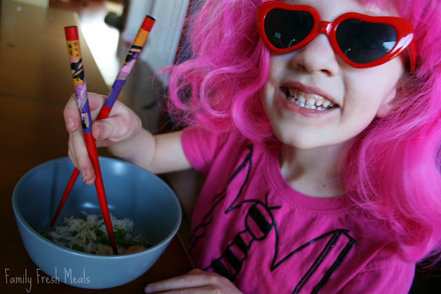 child in a pink wing and sun glasses, eating Coconut Basmati Rice Shrimp with chopstick