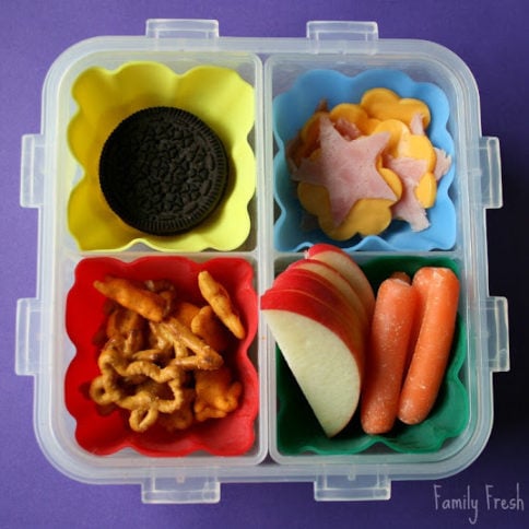Top down image of square lunchbox with cookies, fruit, vegetables, pretzels, ham and cheese
