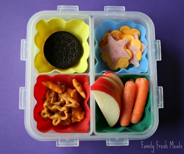 Top down image of square lunchbox with cookies, fruit, vegetables, pretzels, ham and cheese