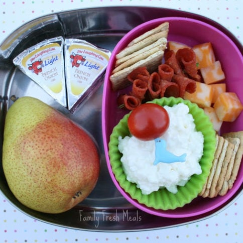 Top down image of a lunch box with a pear, cheese, crackers and pepperoni