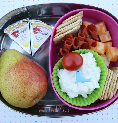 Top down image of a lunch box with a pear, cheese, crackers and pepperoni