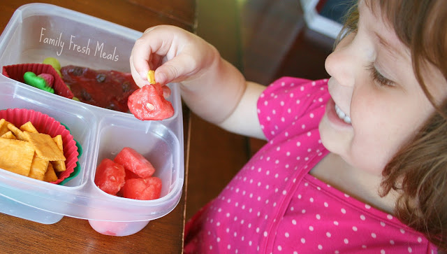 child sitting at a table eating watermelon themed lunchbox