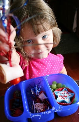 Little girl sitting at table with 4th of July themed lunchbox 