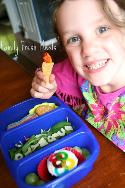 Child sitting with Olympic themed lunchbox, smiling and holding an edible mini torch