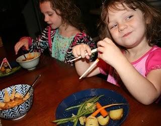 two children sitting at a table eating roasted vegetables