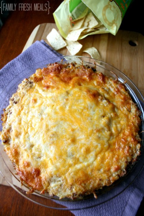 Baked tater tot dip in a glass pie dish with a bag of tortilla chips