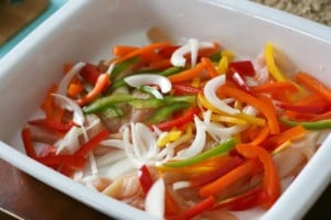 Chicken, bell peppers and onions slices in a white baking dish