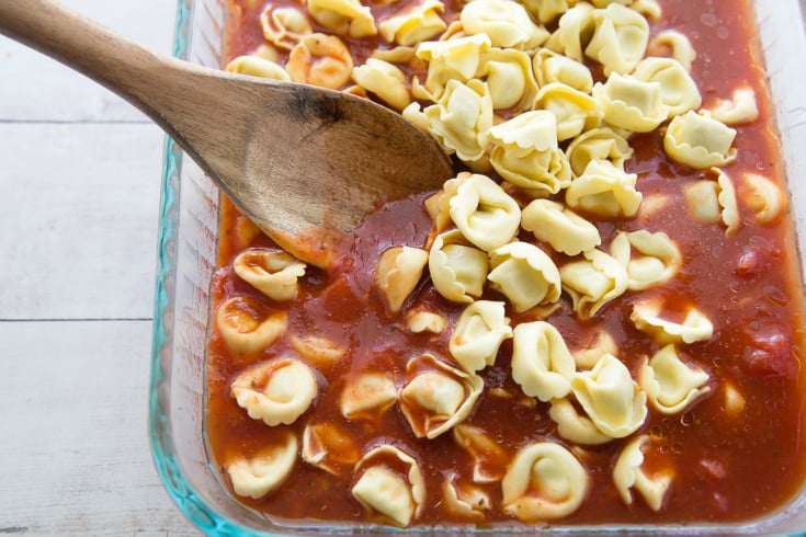 Pasta mixed into a baking pan with sauce and broth