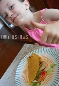 Child sitting at a table with a Chinese Chicken Taco, giving a thumbs up