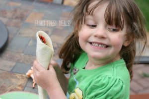 child sitting at a table smiling, while holding a taco