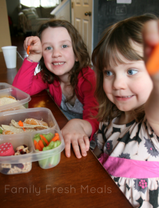 two children sitting at a table with lunchboxes