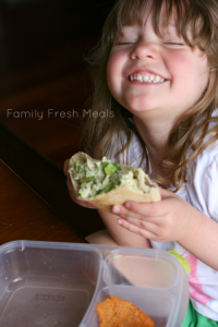 Child smiling, holding a Healthy Avocado Yogurt Chicken Salad pita pocket