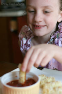 Child dipping Baked Mozzarella Stick in red sauce