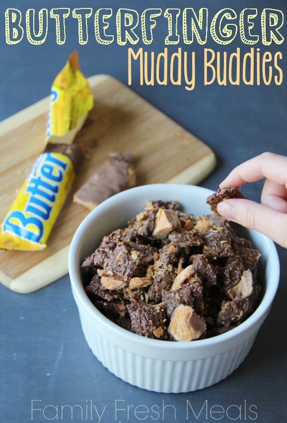 Butterfinger Muddy Buddies Recipe served in a white bowl, with a hand picking up a piece