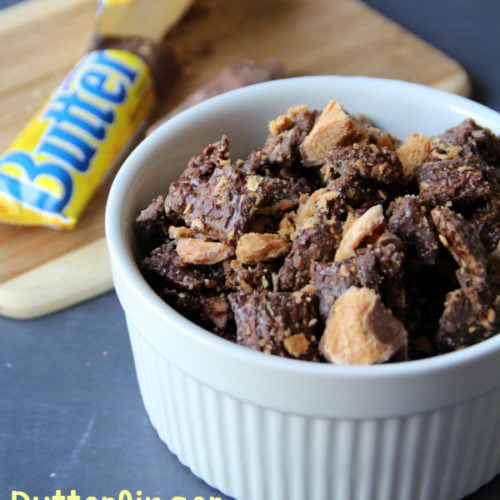 Butterfinger Muddy Buddies Recipe served in a white dish, with an open butterfinger candy car in the background