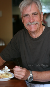 man smiling, sitting at a table with a piece of cake